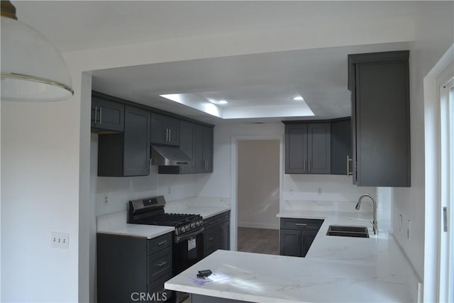 kitchen featuring gas stove, a tray ceiling, under cabinet range hood, a sink, and recessed lighting