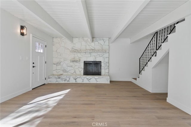 unfurnished living room with a stone fireplace, beamed ceiling, and light wood-type flooring