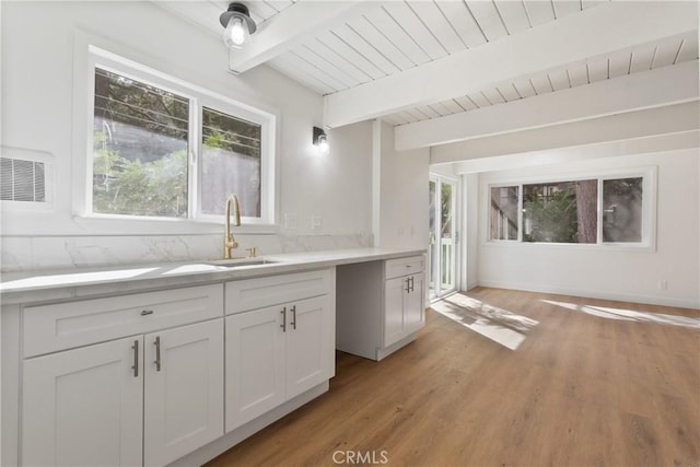 kitchen featuring beamed ceiling, light hardwood / wood-style flooring, white cabinetry, and sink