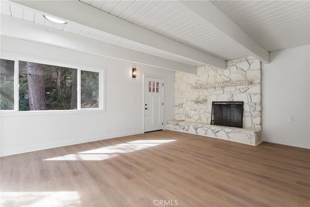 unfurnished living room featuring beamed ceiling, hardwood / wood-style flooring, and a stone fireplace