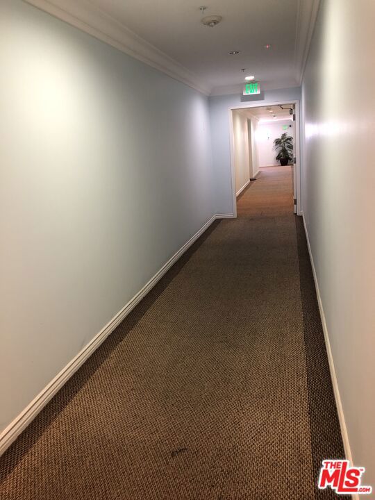 hall with dark colored carpet and crown molding