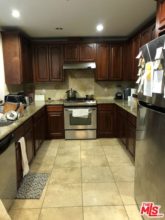 kitchen with light stone counters, light tile patterned floors, appliances with stainless steel finishes, and tasteful backsplash