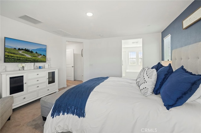 bedroom with ensuite bath and light colored carpet