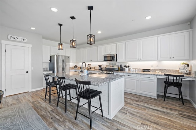 kitchen with white cabinetry, a kitchen bar, an island with sink, appliances with stainless steel finishes, and light stone countertops