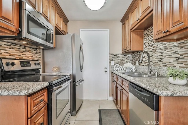 kitchen with tasteful backsplash, light stone counters, stainless steel appliances, sink, and light tile patterned flooring