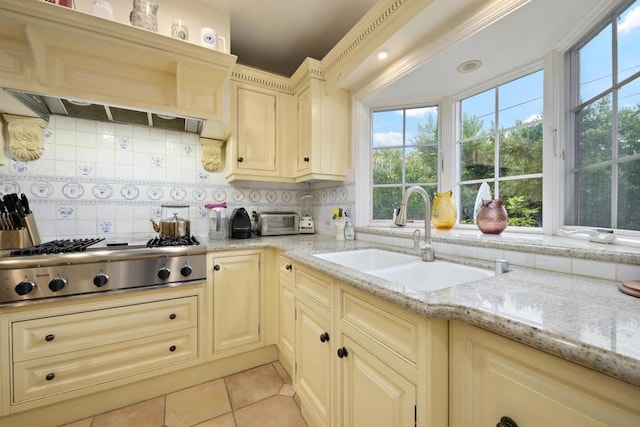 kitchen with backsplash, sink, light stone countertops, and stainless steel gas cooktop