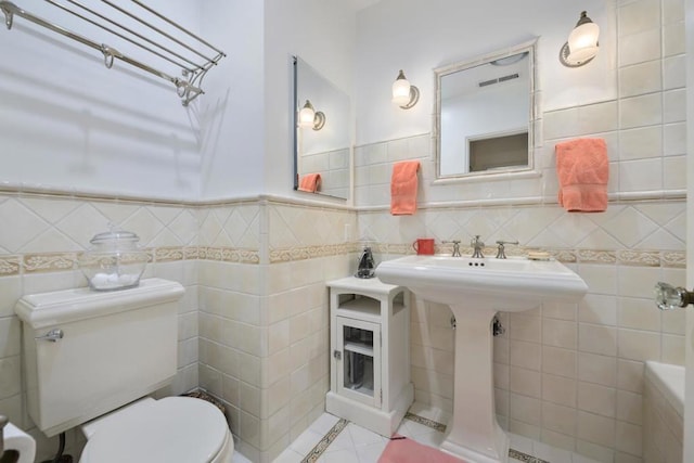 bathroom with toilet, tile patterned flooring, and tile walls