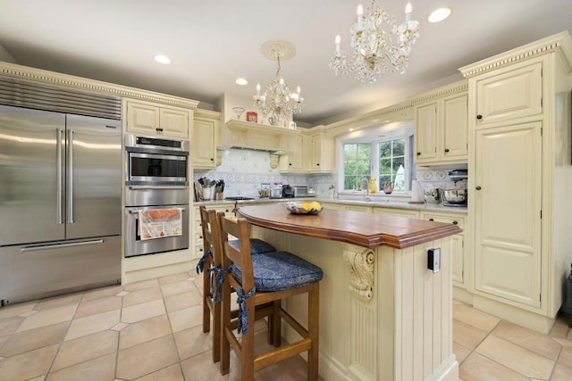 kitchen featuring appliances with stainless steel finishes, decorative light fixtures, wooden counters, a center island, and cream cabinetry