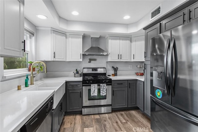 kitchen featuring gray cabinetry, wall chimney range hood, sink, dark hardwood / wood-style flooring, and stainless steel appliances