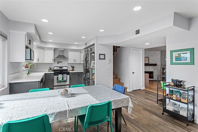 kitchen featuring gray cabinets, dark wood-type flooring, stainless steel appliances, and wall chimney range hood