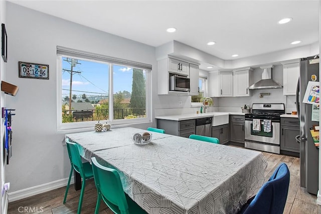 kitchen featuring sink, light hardwood / wood-style flooring, appliances with stainless steel finishes, gray cabinets, and wall chimney range hood