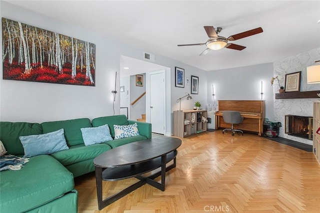 living room featuring a stone fireplace, light parquet floors, and ceiling fan