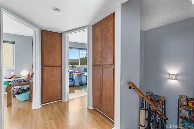 hall with light wood-type flooring and a textured ceiling