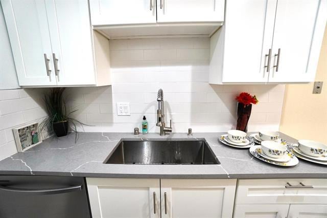 kitchen featuring tasteful backsplash, light stone counters, stainless steel dishwasher, sink, and white cabinets