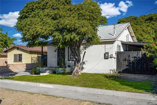 view of front of home featuring a front lawn, roof with shingles, fence, and stucco siding