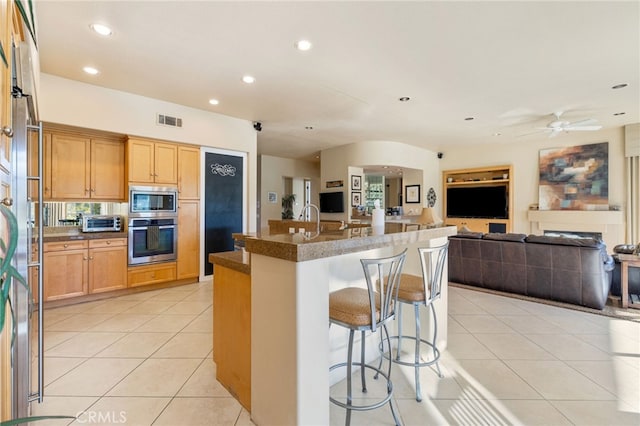 kitchen with light tile patterned flooring, a kitchen bar, a center island with sink, ceiling fan, and stainless steel appliances