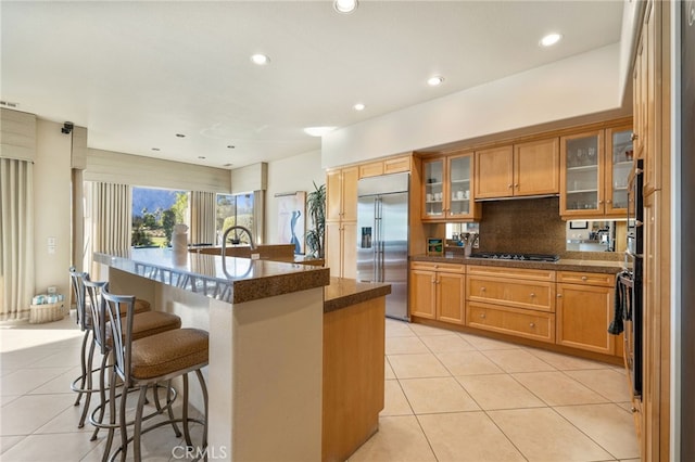 kitchen featuring a kitchen breakfast bar, an island with sink, built in fridge, black gas stovetop, and decorative backsplash