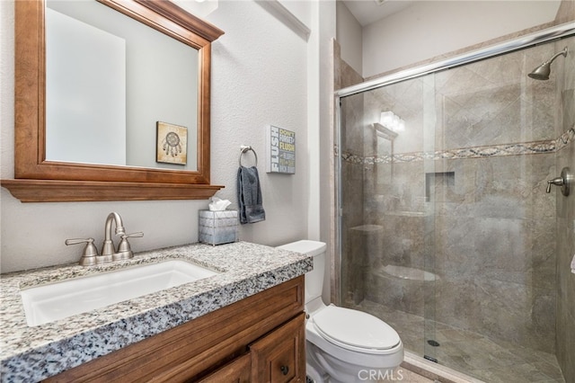 bathroom featuring a shower with door, vanity, and toilet