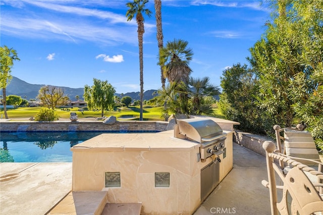 view of pool featuring an outdoor kitchen, a grill, a mountain view, and a patio area