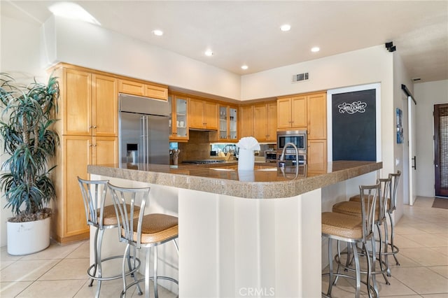 kitchen with backsplash, a kitchen bar, light tile patterned floors, built in appliances, and a spacious island