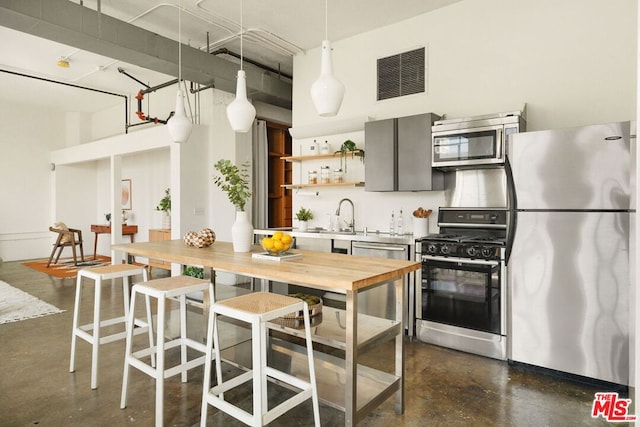 kitchen featuring appliances with stainless steel finishes, a towering ceiling, pendant lighting, and sink