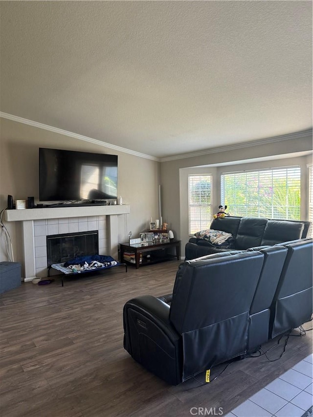 living room featuring a tiled fireplace, crown molding, hardwood / wood-style floors, and a textured ceiling