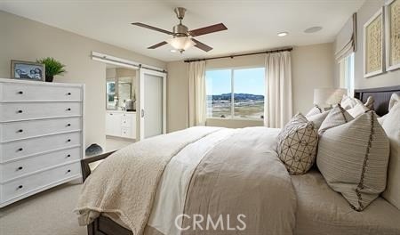 bedroom with connected bathroom, a barn door, ceiling fan, and light colored carpet