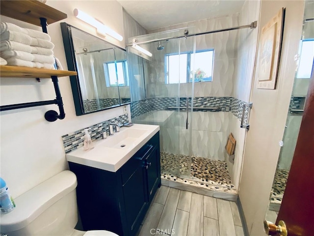 bathroom with vanity, tasteful backsplash, toilet, and a shower with door