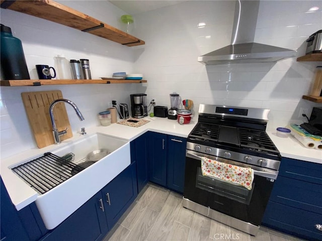 kitchen featuring blue cabinetry, stainless steel gas stove, sink, wall chimney range hood, and decorative backsplash