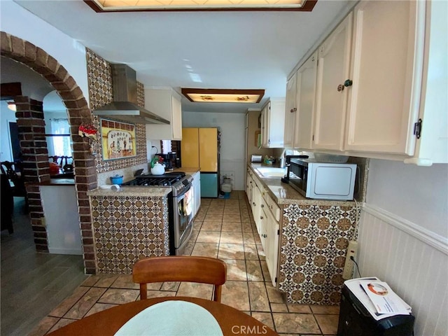 kitchen featuring light wood-type flooring, sink, wall chimney range hood, stainless steel gas stove, and white cabinetry