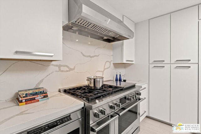 kitchen with white cabinetry, double oven range, light stone countertops, and wall chimney exhaust hood