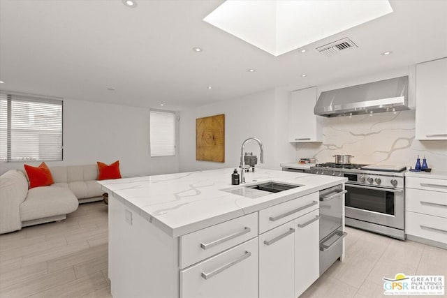 kitchen featuring white cabinetry, sink, a kitchen island with sink, stainless steel range, and wall chimney exhaust hood