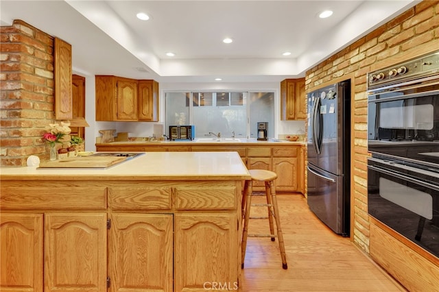 kitchen with brick wall, double oven, kitchen peninsula, stainless steel fridge, and light hardwood / wood-style floors