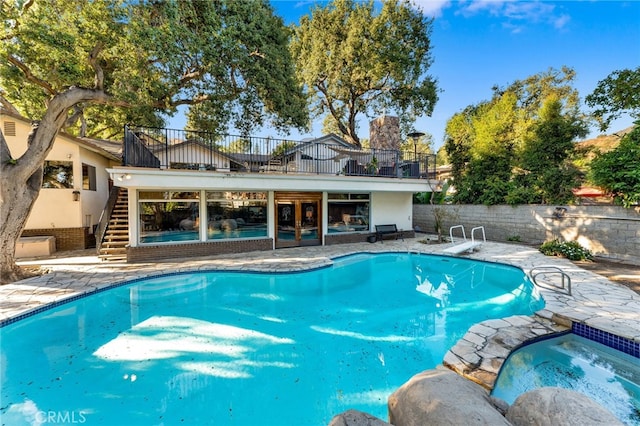 view of pool featuring fence, a pool with connected hot tub, stairs, a diving board, and a patio area