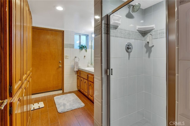 bathroom with hardwood / wood-style flooring, vanity, a shower with shower door, and tile walls