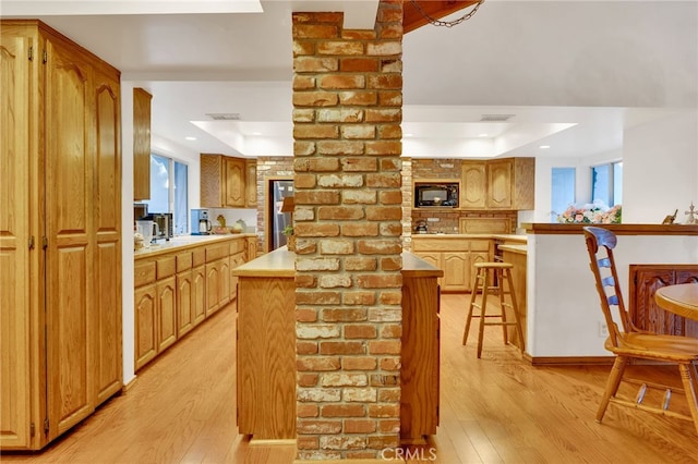 kitchen with black microwave, a peninsula, a breakfast bar, light countertops, and stainless steel refrigerator