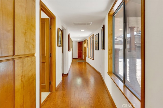 corridor with light wood-style floors, visible vents, and baseboards