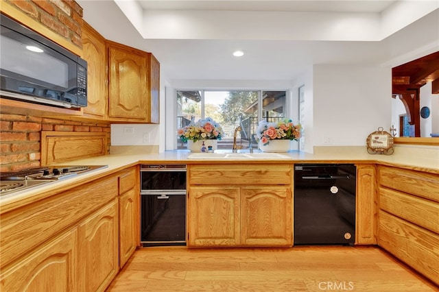 kitchen with black microwave, light wood-style flooring, a sink, gas stovetop, and light countertops