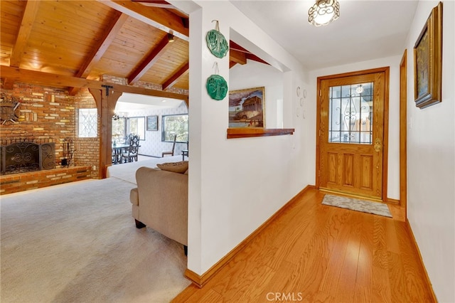 entryway with vaulted ceiling with beams, a fireplace, wood ceiling, baseboards, and light wood-type flooring