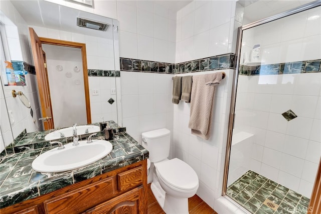 bathroom with toilet, a stall shower, vanity, and tile walls