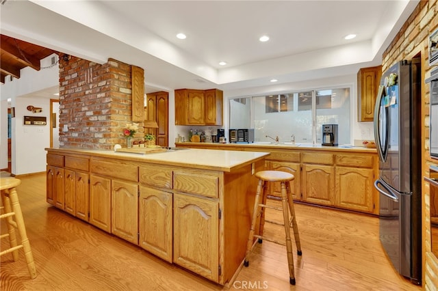 kitchen with a kitchen bar, stainless steel fridge, light hardwood / wood-style flooring, and a kitchen island