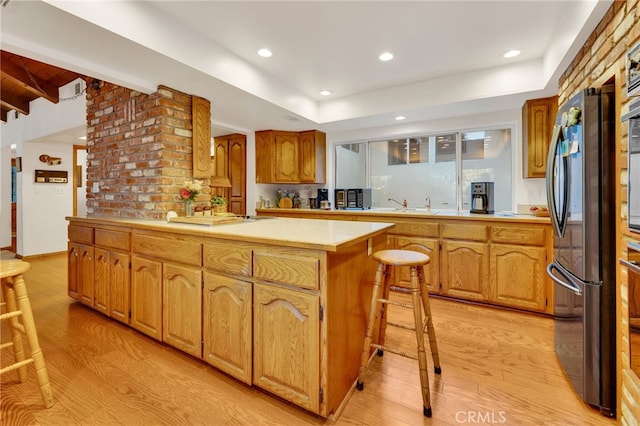 kitchen featuring a kitchen breakfast bar, light countertops, freestanding refrigerator, a center island, and light wood finished floors