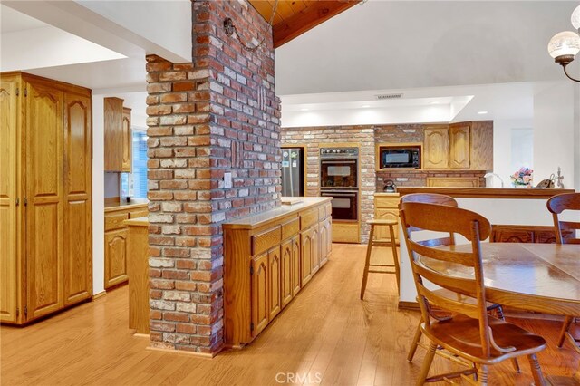 kitchen featuring beamed ceiling, black appliances, brick wall, and light hardwood / wood-style floors