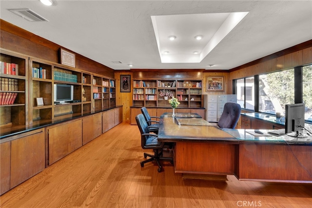 home office with light wood-style flooring, visible vents, and a tray ceiling