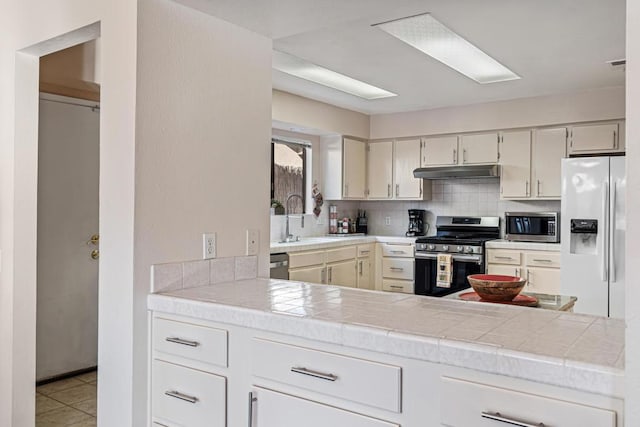 kitchen featuring tile countertops, sink, decorative backsplash, light tile patterned floors, and appliances with stainless steel finishes