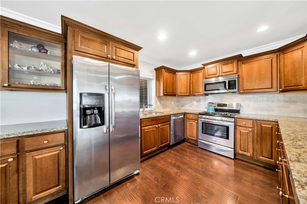 kitchen featuring decorative backsplash, stainless steel appliances, light stone counters, and dark wood-type flooring