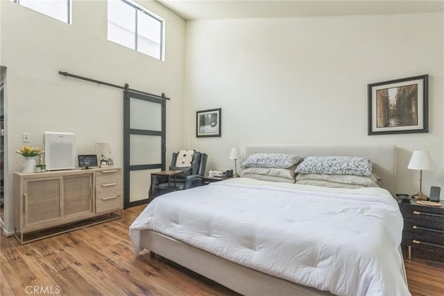 bedroom featuring a barn door, a towering ceiling, and hardwood / wood-style flooring