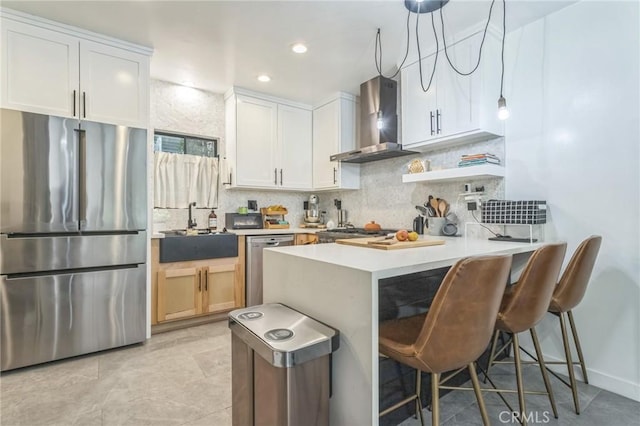 kitchen featuring wall chimney exhaust hood, kitchen peninsula, pendant lighting, white cabinets, and appliances with stainless steel finishes