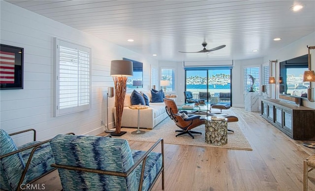 living room with ceiling fan, wooden walls, and light wood-type flooring