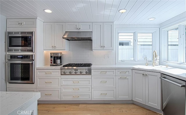 kitchen featuring sink, ventilation hood, backsplash, appliances with stainless steel finishes, and light wood-type flooring